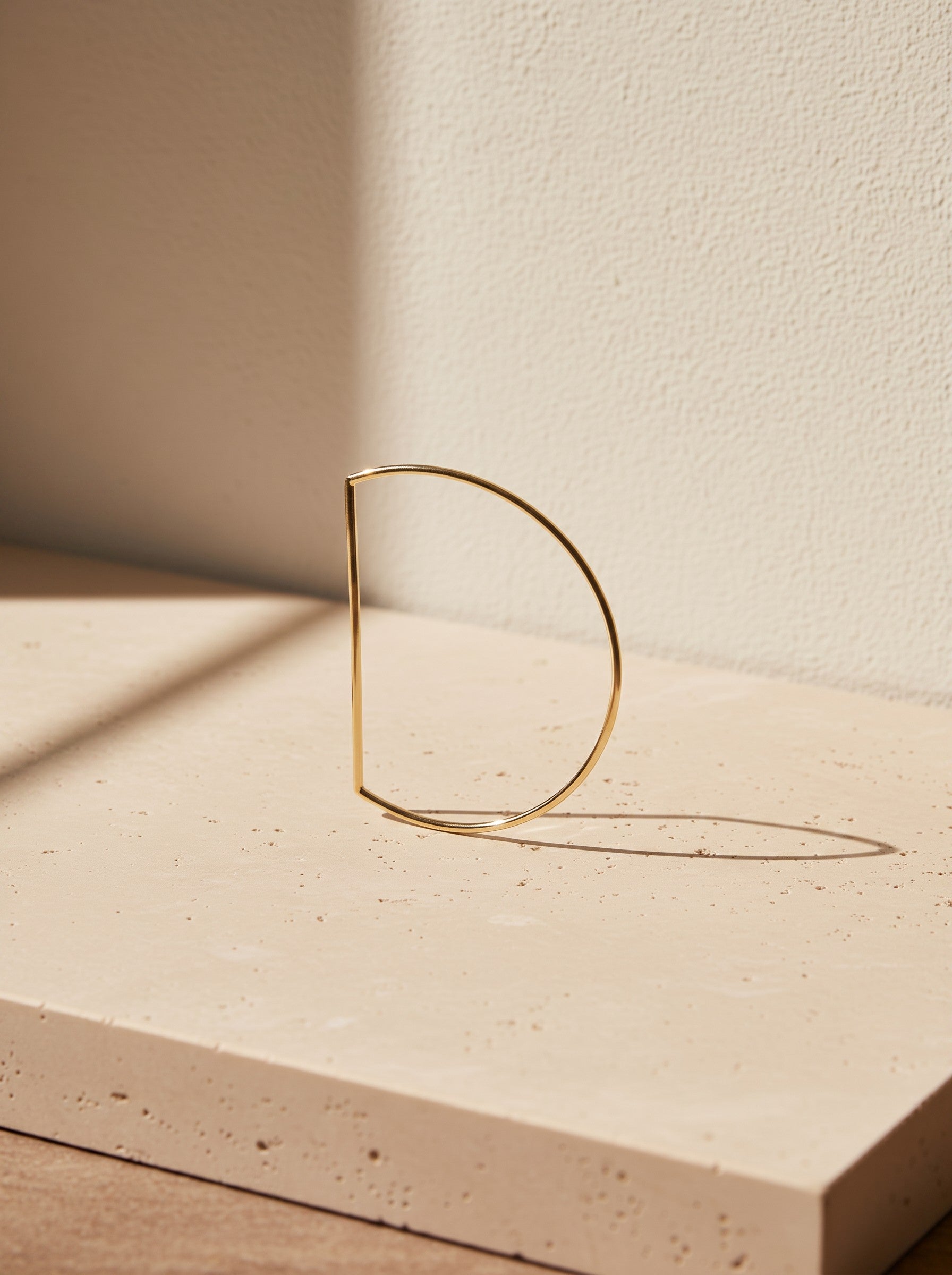 Gold-tone Anito D-shaped bangle styled on a warm limestone surface in natural light.