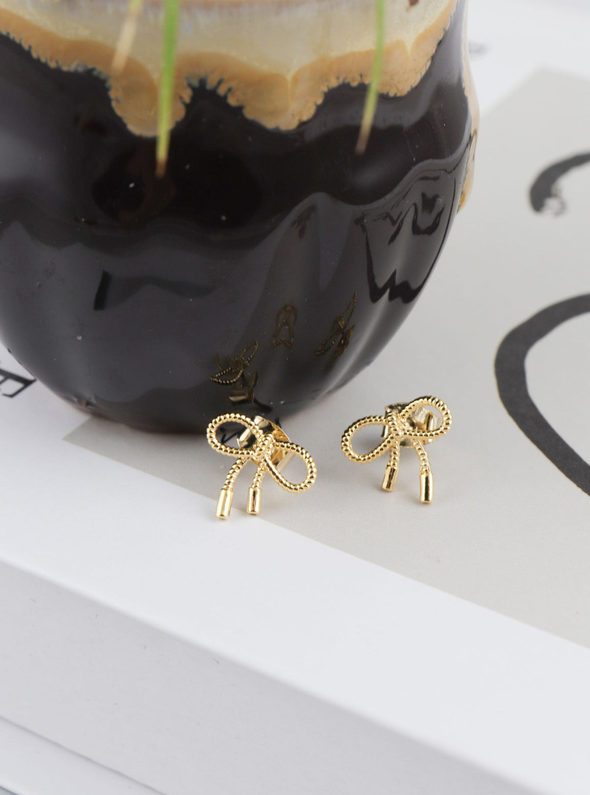 Tavora gold bow stud earrings styled beside a ceramic vase