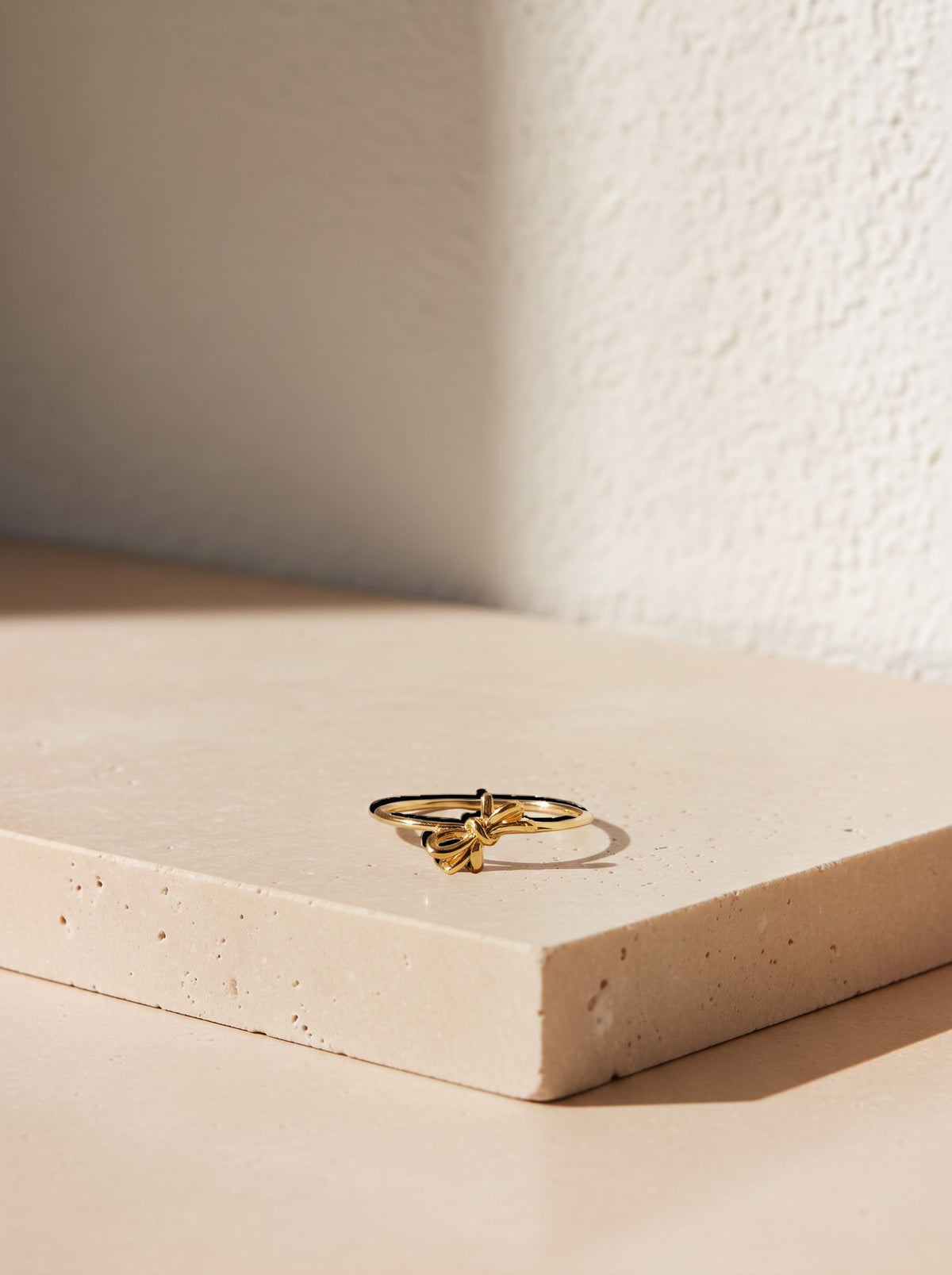 Gold Melandia bow ring styled on warm limestone.