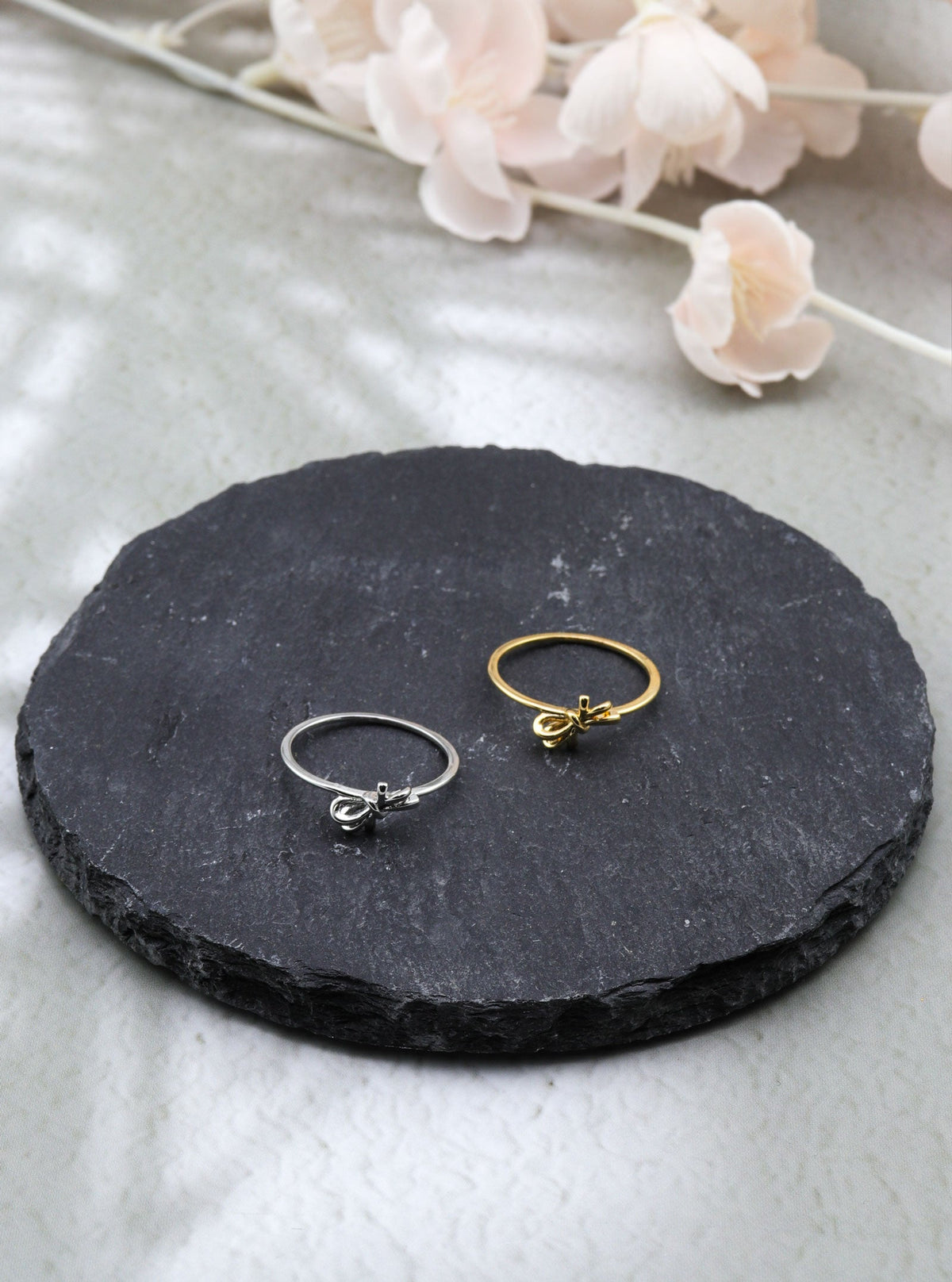 Gold and silver Melandia bow rings displayed on black slate.