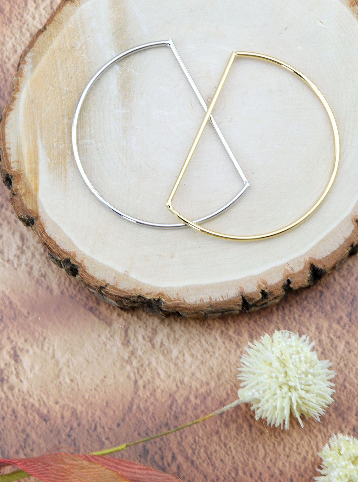 Gold and silver-tone Anito D-shaped bangles styled together on a natural wood slice.